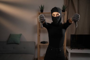 Mutsuz bir hırsız ya da siyah kar maskeli davetsiz bir misafir. Bir evin içinde, baş parmak göstererek hoş olmayan bir jesti işaret ediyor. Hırsızlık, suç, hırsızlık ve soygun kavramı. Boşluğu kopyala