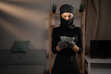 Kar maskesi takan kadın hırsız. Gece evde para sayıyor. Boşluğu kopyala