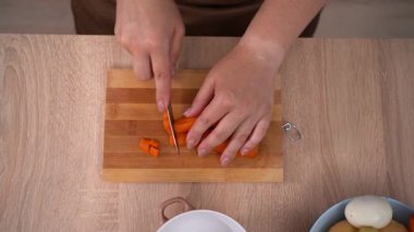 Keskin bir bıçak kullanan kadın eli tahta kesme tahtasında haşlanmış havuç kesiyor. Haşlanmış sebze salatası için malzeme hazırlıyorum. Yakın plan. Üst görünüm