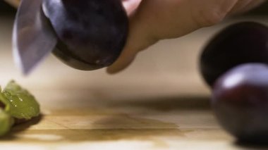 Kadın ellerine yakın çekim. Olgun erikleri, ahşap tahtada bıçakla keserek doku ve detayı gösteriyor. Boşluğu kopyala