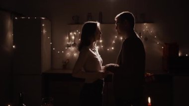 Sevgililer Günü 'nü veya yıldönümünü birlikte evde, samimi bir aşk ortamında geçirirken öpüşen ve hediyeleşen romantik bir çiftin silüeti.