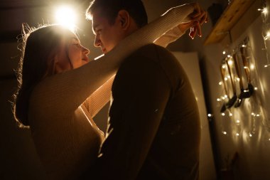 Aşıkların silueti gece mutfakta arka plandaki ışıkların çelenklerine sarılıyor. Boşluğu kopyala