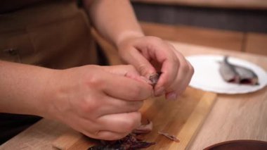 Kadın ellerinin tuzlanmış balıktan kemikleri çıkarırken mutfak içinde yemek pişirme, deniz ürünleri temizliği ve geleneksel ev yapımı yemek hazırlama kavramını kapatması.