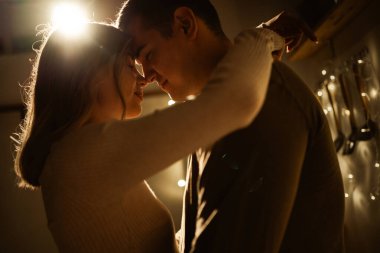 Sarılıp öpüşen genç bir çiftin yakın çekimi. Sevgililer gününü evde romantik tutku ve şefkatin akşam atmosferinde kutluyoruz. Boşluğu kopyala