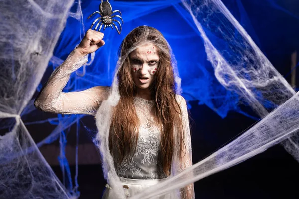 Korkunç Cadılar Bayramı zombi makyajlı uğursuz kadın kameraya yumruk sallayarak korkutmaya çalışıyor. Örümceğin arka planında ölü kadın izleri var. Boşluğu kopyala