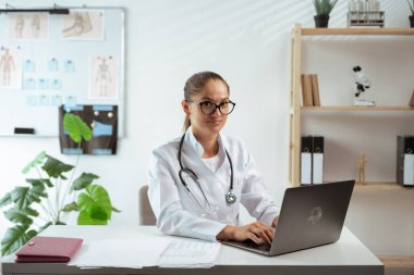 Hastanede dizüstü bilgisayarlı gülümseyen kadın doktorun portresi. Online danışma ve teletıp konsepti