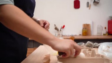 Woman chef cracks fresh eggs in the glass bowl cooking breakfast in the kitchen. side view
