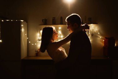 Birbirine aşık çiftlerin silueti geceleri mutfakta çelenk ışıklarının arka planına sarılıyor. Romantik anlar. Aşk ve tutku kavramı.