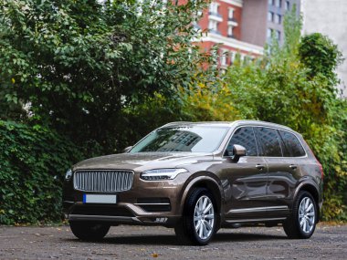 Parlak bir yaz gününde, büyük alaşımlı tekerlekleri ve LED farları olan modern kahverengi SUV aracı şehirde bir otoparkta.
