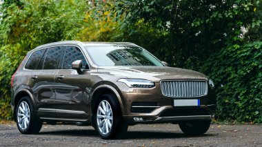 Parlak bir yaz gününde, büyük alaşımlı tekerlekleri ve LED farları olan modern kahverengi SUV aracı şehirde bir otoparkta.