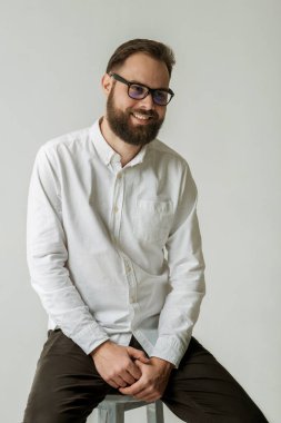 Beyaz gömlek ve gözlük takan neşeli gülüşlü yakışıklı bir adamın stüdyo portresi. Modelin beyaz arka planda izole edilmiş güzel uzun bir sakalı var.