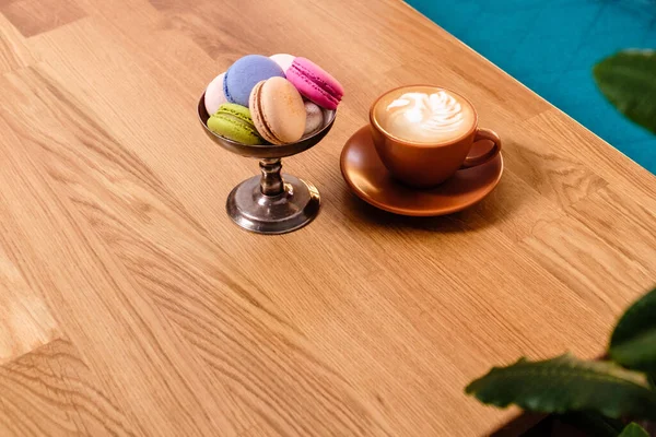 金属製の器の中のマカロンとカフェの木のテーブルの上のコーヒー — ストック写真