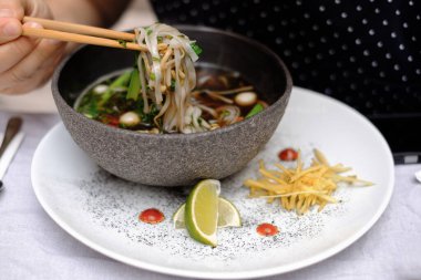 Geleneksel Vietnamlı pho bo çorbası sebzeli ve siyah kasede erkek eli çubuklu et.