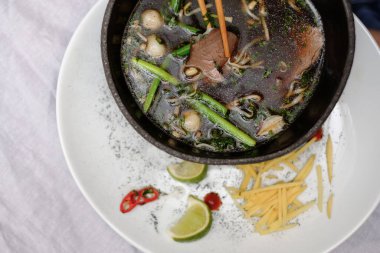 Geleneksel Vietnam pho bo çorbası sebzeli ve siyah kasede beyaz tabakta sığır eti.