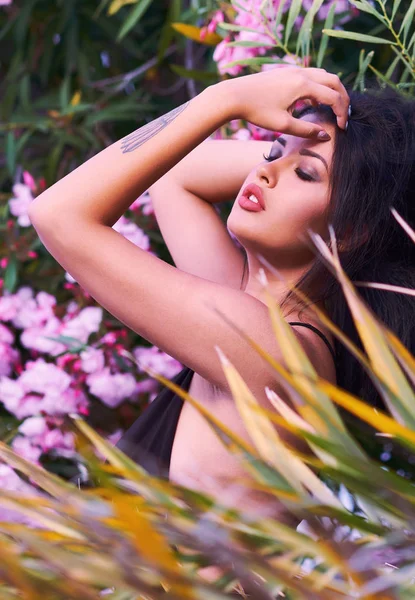 Kafa rüya açık havada poz gözlü esmer kadın kapalı seksi genç portresi vurdu. Kız poz çiçeklenme parlak güzel pembe çiçekler ve yapraklar. 20-25 yaşında erkek. Romantik, duygusal ruh hali, summertim