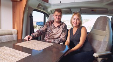 Married middle age couple sitting inside of recreational vehicle looking at camera. Active people lifestyle, adventure and journey, traveling the world in a camper van concept clipart