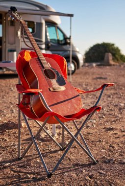 Dikey görünüm kırmızı eğlence araç karavan römork, hiçbir insan yakın bir katlanan sandalyede akustik gitarda. Hobi seyahat ve yaşam tarzı kavramı