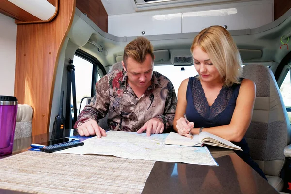 Middle aged married couple talking about future adventure planning route looking at map sitting inside of recreational vehicle motor home trailer. Active lifestyle, traveling by motor vehicle concept