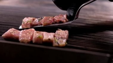 Şef balık dilimleri pişiriyor, siyah eldivenli adam metalik spatula tutuyor terbiye edilmiş cerrahların parçalarını iki sıra halinde barbekü ızgarasının sıcak yüzeyine koyuyor, yavaş çekim videosu erkek elini kapatıyor.