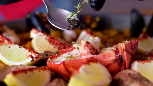 Hand des Küchenchefs mit Kochlöffel dekoriert Paella mit schwarzem Kaviar, Zeitlupe Nahaufnahme Video, reife Zutaten der zubereiteten Paella serviert spanische traditionelle Küche