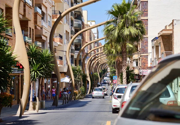 Busy Caballero de Rodas street Torrevieja resort town unusual bended street lights along the urban road in the center of city, lush palm trees walking people, Spain — Stock Photo, Image