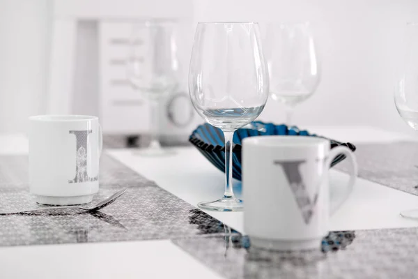 On a white kitchen dining table on place mat tea cups close up focus on empty transparent clear wine glass at the cozy modern room — Stock Photo, Image