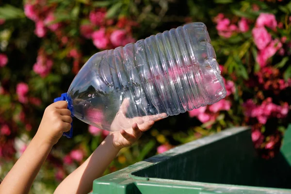 Fechar as mãos de criança pequena segurando vazia grande garrafa de plástico de água jogando em lixeira — Fotografia de Stock