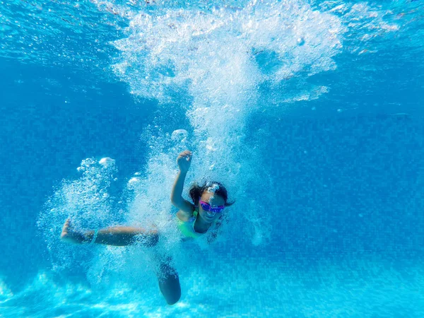 Kleines Mädchen von Blasen umgeben fällt in blaues Wasser des Schwimmbades — Stockfoto