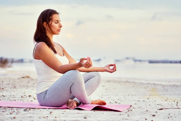 Alone yogi woman seated in lotus position meditating near lake — Stock Photo, Image