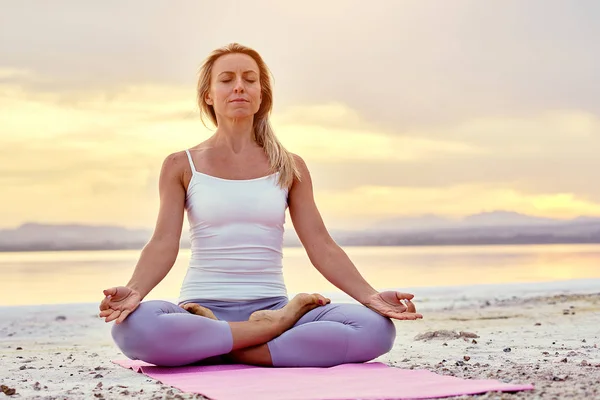 Middle-aged woman seated in lotus pose doing meditation on naturure — Stock Photo, Image