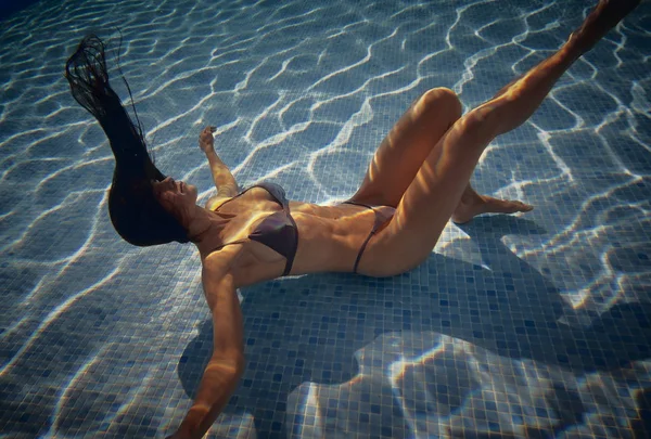 Ung kvinna som simmar poserar orörlig inuti poolen — Stockfoto