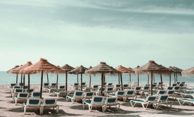 Bulutlu gökyüzü Akdeniz sularını sakinleştirdi. İspanya 'nın Malaga Eyaleti' nin kumlu sahilinde saman şemsiyeleri altında sıralanmış boş güverte sandalyeleri güneşlendi.