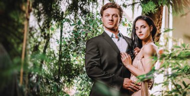 Güzel, genç ve aşık bir çift. Yeşillik ormanında ayakta duruyor. Doğa el ele tutuşuyor. Zarif bir gece elbisesi giyen adam resmi takım elbise giyiyor. Sevgili fotoğraf çekimi konsepti