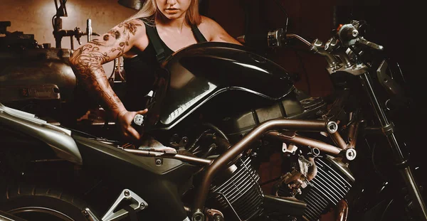 年轻强壮的金发白人机修工女人 带着纹身的胳膊 穿着工作服 独自在车间修理摩托车 剪接概念摄影 生活方式 — 图库照片