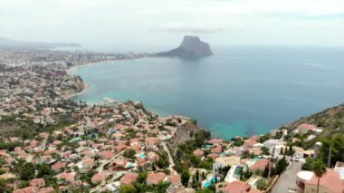 İnsansız hava aracı bakış açısı Calpe veya Calp kasabasının çatıları parlak Akdeniz suları ve Park doğal Penon de Ifach veya Penyal de Ifac kayaları, bulutlu gökyüzü. Costa Blanca, İspanya