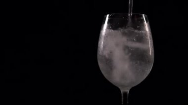 Kabarcıklar ve köpüklü köpüklü köpükler, siyah arka planda şarap kadehinde. Soda içeceği, şeffaf bardağa dökülüyor. Yavaş çekim, yakın görüntü.