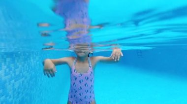 Yavaş çekim manzaralı, 7-8 yaşlarında bir kız mayo giyer ve suya batırılmış gözlük takar yaz tatillerinde havuzda yüzer. Aktif yaşam tarzı ve spor etkinliği kavramı