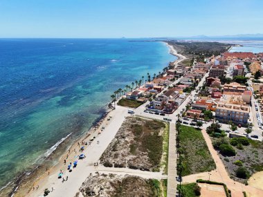 İspanya 'nın Torre de la Horada kıyı şeridinin insansız hava aracı görüntüsü, altın kumlu plajlar, turkuaz Akdeniz suları, renkli şemsiyeler, kıyı boyunca canlı yerleşim alanları. Costa Blanca, İspanya