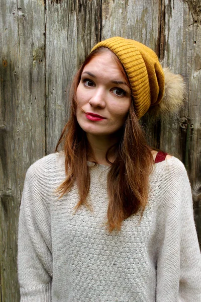 woman smiles in a sweater and a hat with a pompon.