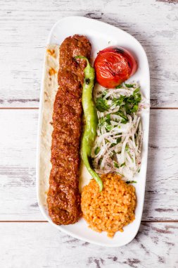 Adana Kebap beyaz tabak içinde yeşil sebzeler ile servis
