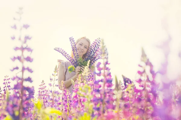 Vacker och glad kvinna med bukett av lupiner på fältet — Stockfoto