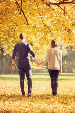 Genç çift sonbahar parkında yürüyor.