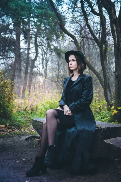 Chica en un abrigo negro sentado en un banco —  Fotos de Stock