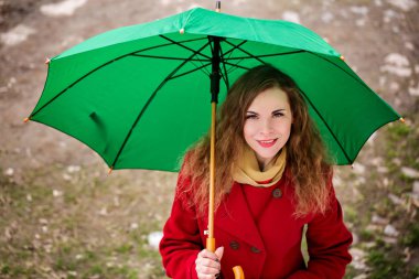 Güzel kadın kırmızı paltolu bir yeşil şemsiye tutan
