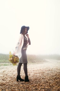 Şapkalı güzel bir kız sonbahar ormanın üzerinde yürüyor