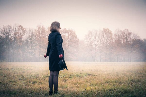 Женщина в черном пальто и шляпе в туманную погоду
