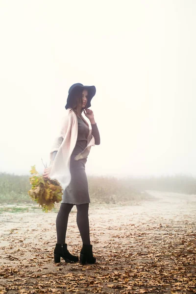 Şapkalı güzel bir kız sonbahar ormanın üzerinde yürüyor