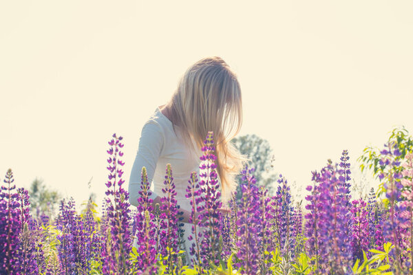 Beautiful blonde young woman in a field with blooming lupines