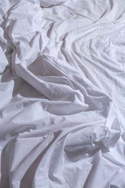a crumpled white bed in the morning light