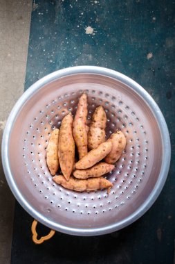 Karanlık bir arka plan üzerinde metal bir kevgir içinde turuncu tatlı patates